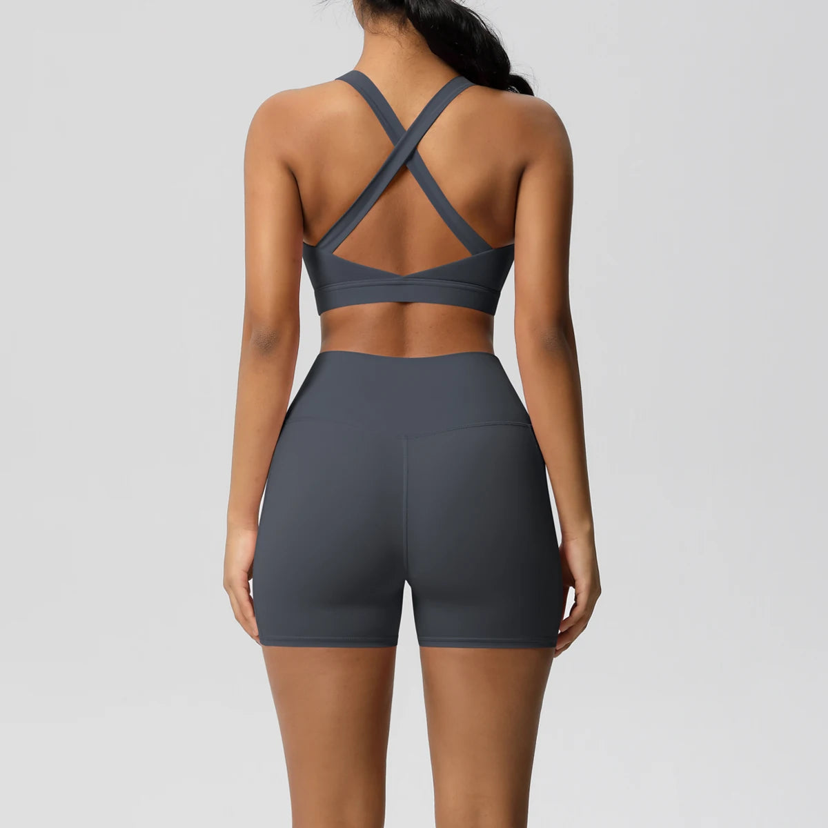 Two-piece women's sportswear yoga set with crossover bra, pocketed gym shorts, and matching leggings for active fitness wear.