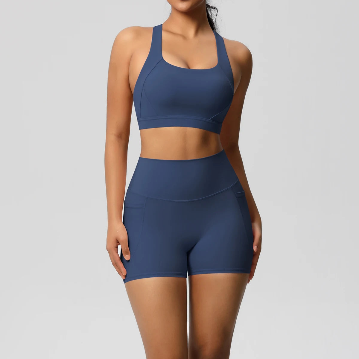 Two-piece women's sportswear yoga set with crossover bra, gym shorts, and leggings, featuring pockets and a sleek fitness design.
