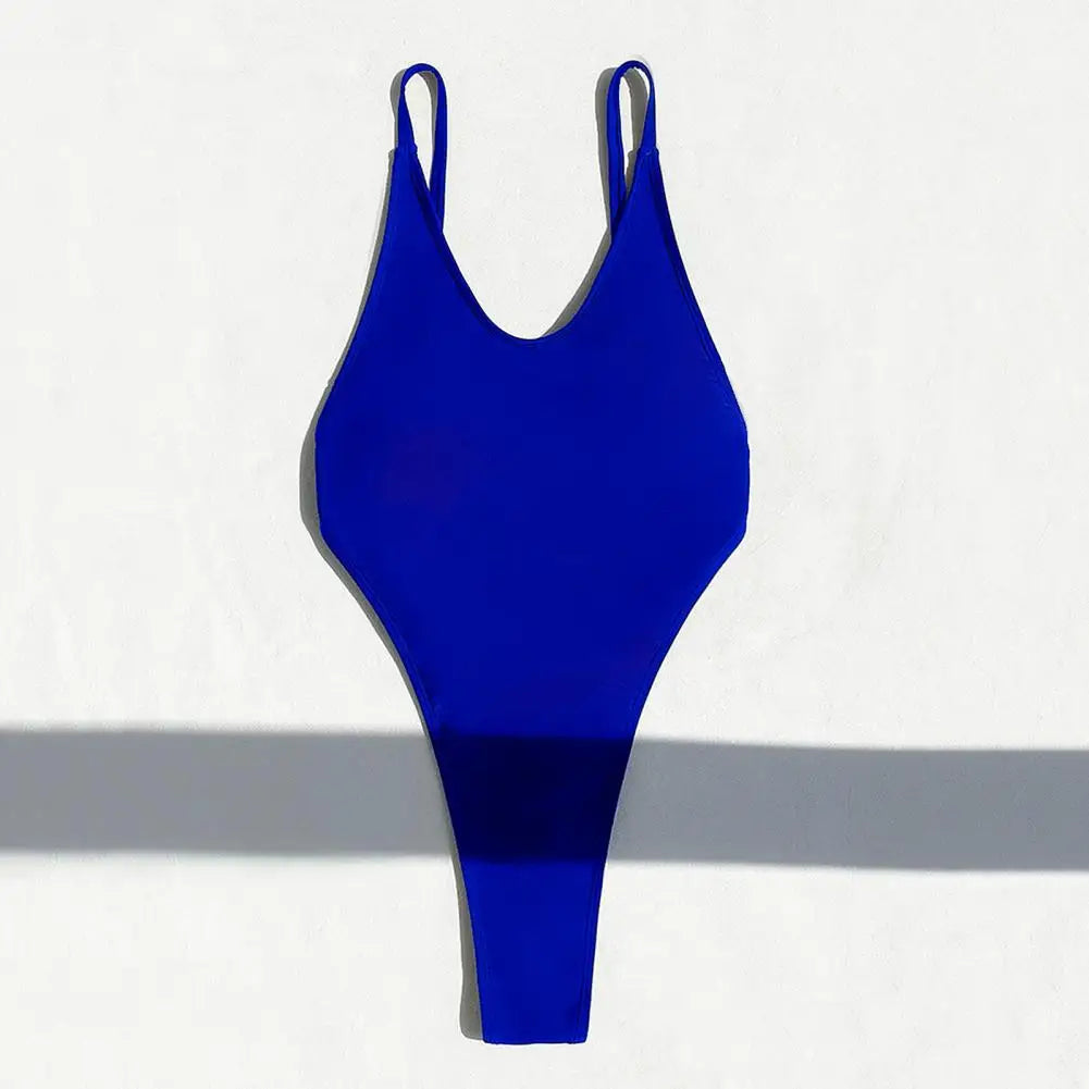Backless micro thong one-piece swimsuit for women by The Clothing Company Sydney, shown on a model in a beach setting.