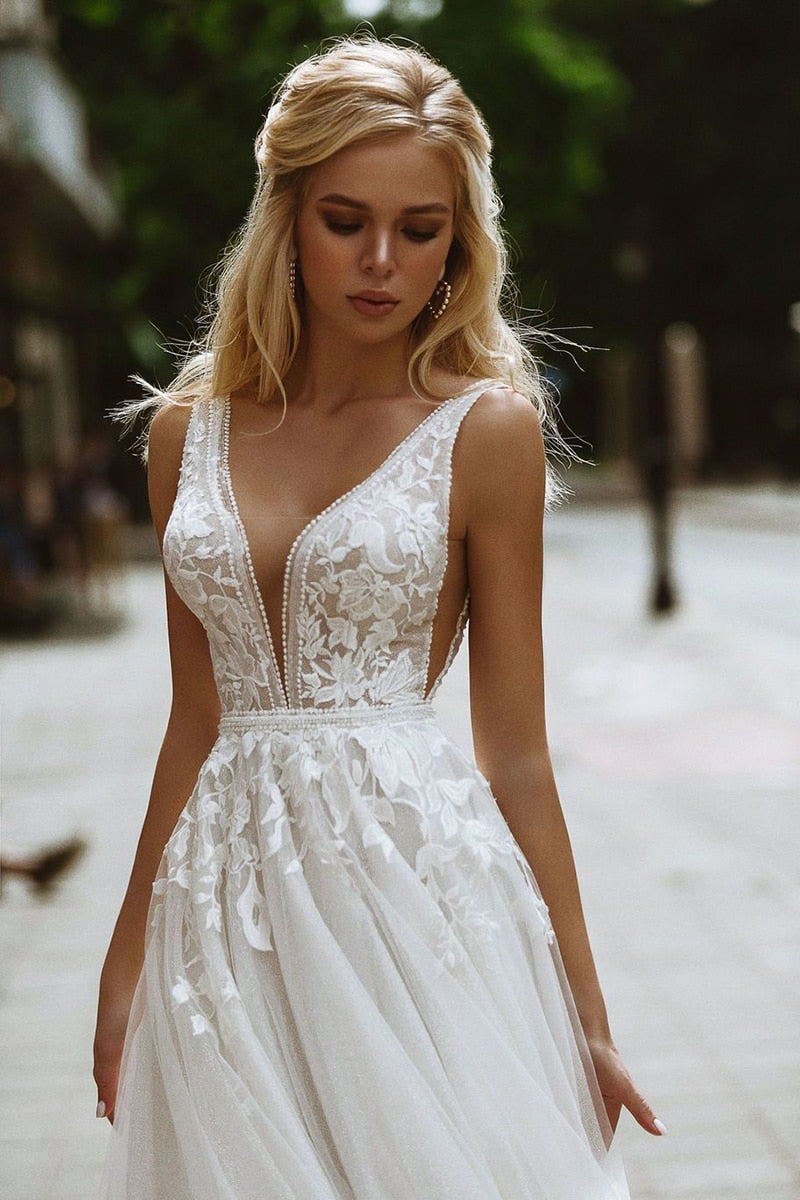 Boho wedding dress by The Clothing Company Sydney featuring deep V-neck, lace appliques, pearl buttons, tulle skirt, and A-line silhouette.
