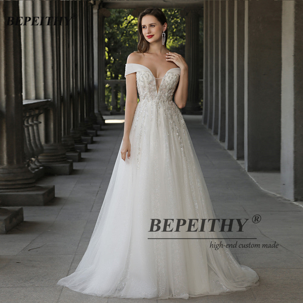 Off-the-shoulder ivory boho wedding dress by The Clothing Company Sydney, lace and beading A-line bridal gown for UK brides.