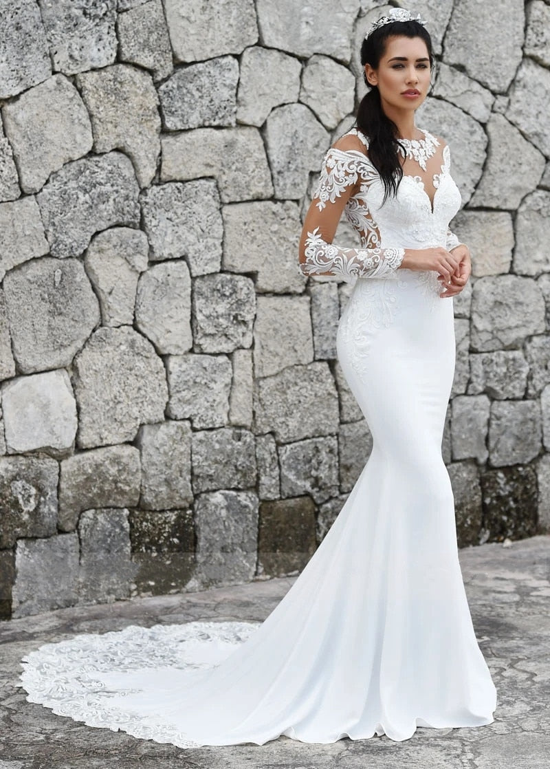 Elegant mermaid wedding dress with long sleeves, illusion back, lace appliqué, button details, and a flowing train.