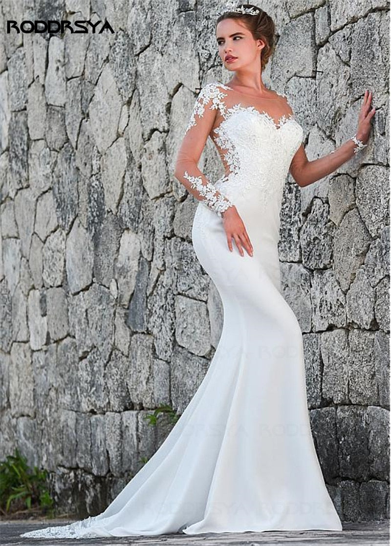 Long sleeve sheer lace appliqué mermaid wedding dress with see-through back and button details, designed by The Clothing Company Sydney.