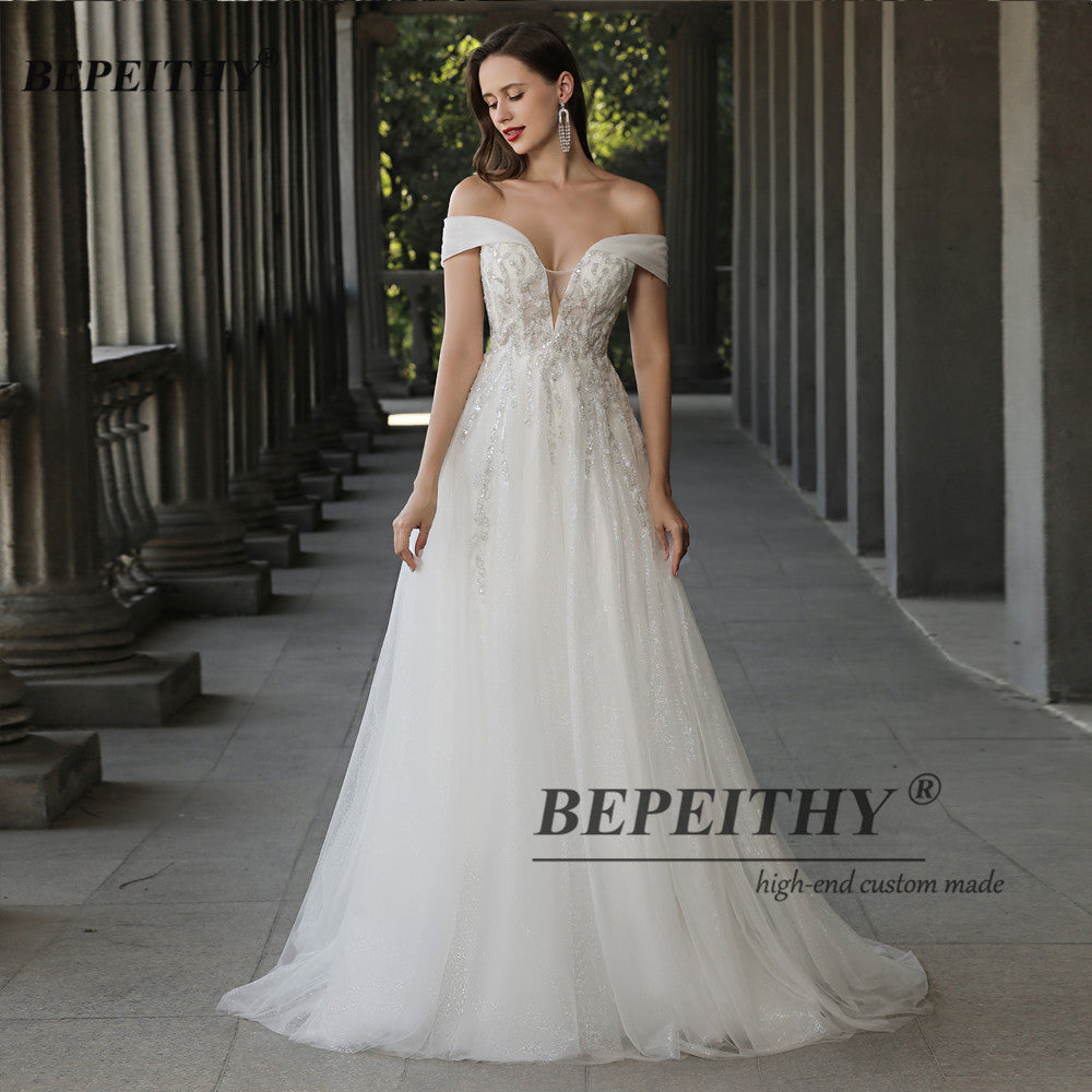 Ivory off-the-shoulder boho wedding dress with lace, beading, and A-line silhouette, designed by The Clothing Company Sydney.