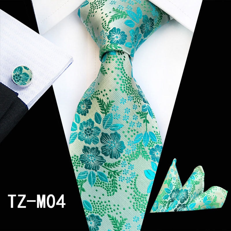 Men's silk tie set including red and green floral necktie, matching handkerchief, cufflinks, and accessories for business or wedding wear.