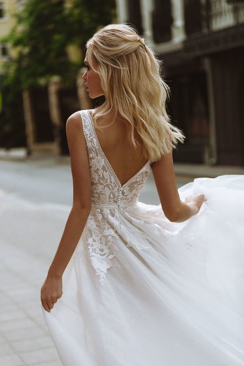Boho wedding dress by The Clothing Company Sydney featuring deep V-neck, lace appliques, pearl buttons, tulle A-line gown.
